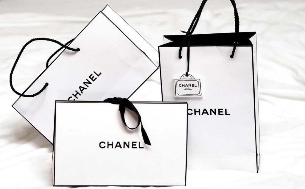 des sacs de shopping noir et blanc de la marque de luxe Chanel sur un lit
